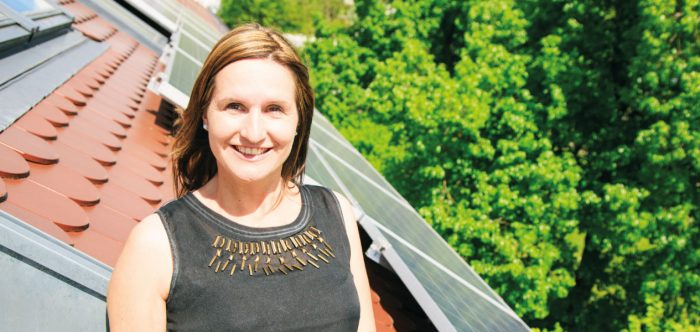 A woman proudly standing in front of solar panels on the roof of her home