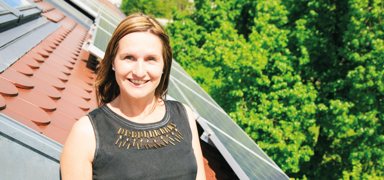 A woman proudly standing in front of solar panels on the roof of her home