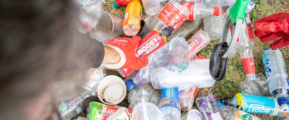 Close up of bottles and litter and cans with hand picking up a bottle