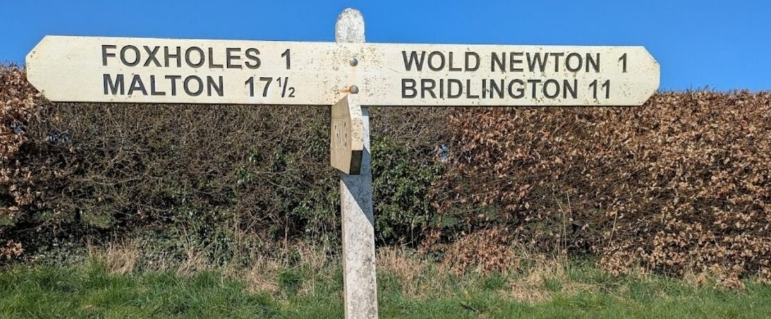 A wooden signpost with directions to Foxholes (1 mile), Malton (17.5 miles), Wold Newton (1 mile) and Bridlington (11 miles)