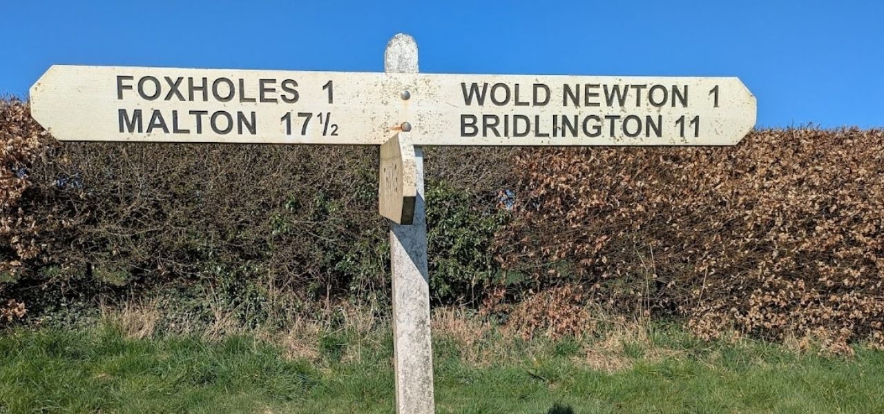 A wooden signpost with directions to Foxholes (1 mile), Malton (17.5 miles), Wold Newton (1 mile) and Bridlington (11 miles)