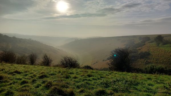 Mist rising from the rolling hills with a hazy sun behind some clouds.