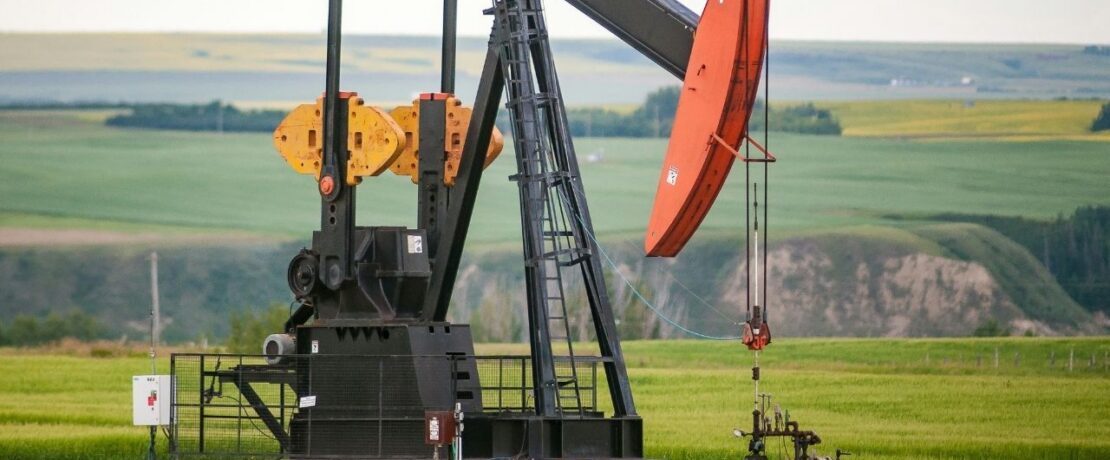 2. A solitary oil pump operates in a wide, open field, surrounded by grass and distant trees.