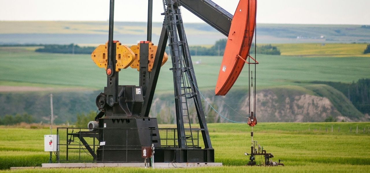2. A solitary oil pump operates in a wide, open field, surrounded by grass and distant trees.